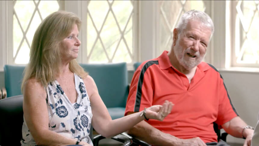 Video play button with an image of someone living with Parkinson’s and his care partner